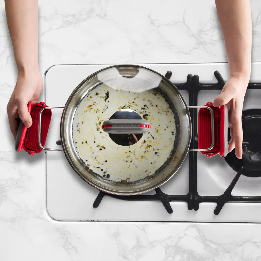 Clipping red pebblegrip onto double handle cookware while it is cooking on a gas hob