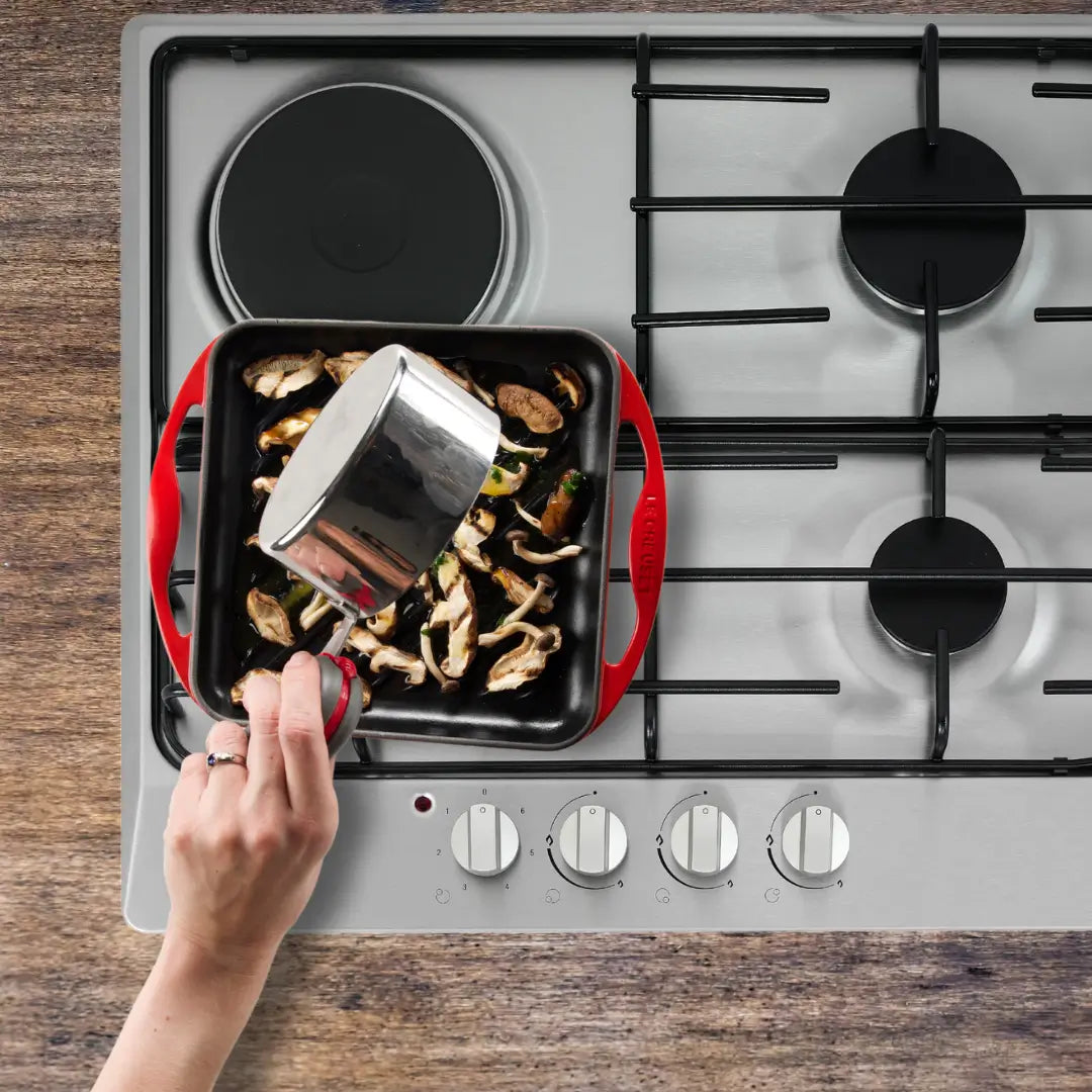 Pouring sauce over mushrooms on red Le Creuset griddle plate, using PebbleGrip to hold the hot saucepan handle.