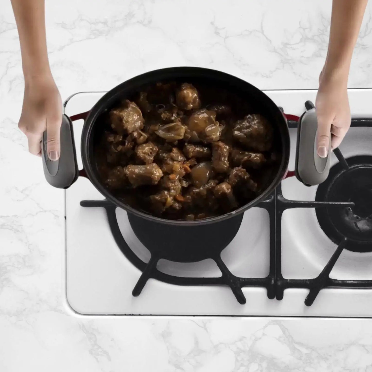 PebbleGrip heat-resistant grips protecting hands while lifting a hot cast iron pot on a stovetop